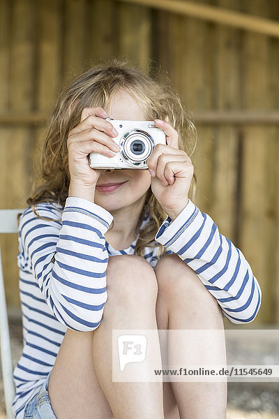 Lächelndes blondes Mädchen beim Fotografieren mit einer Digitalkamera