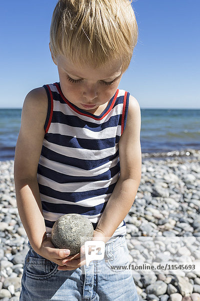 Porträt eines blonden Jungen mit Stein am Strand