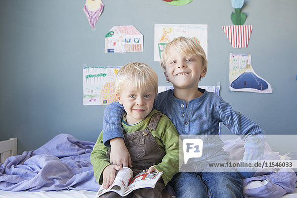Porträt von zwei kleinen Brüdern  die auf dem Bett des Kinderzimmers sitzen.