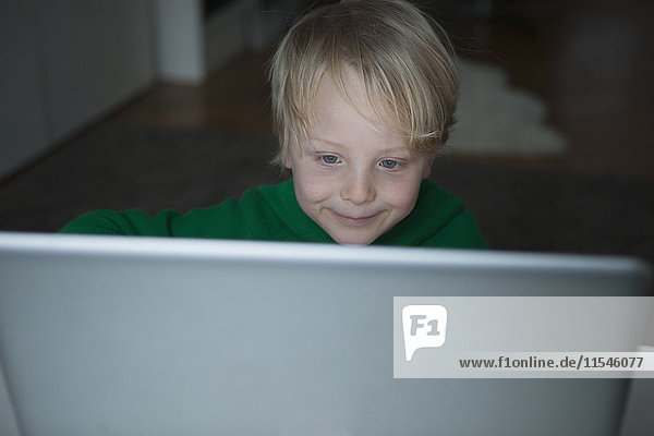 Porträt eines lächelnden blonden Jungen  der auf den Computer schaut