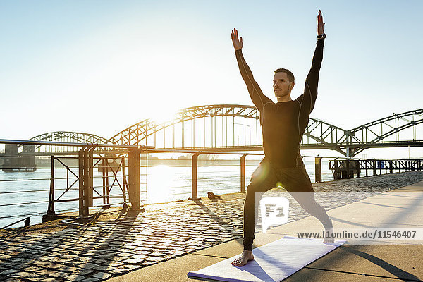 Germany  Cologne  Young man practicing yoga at the riverside