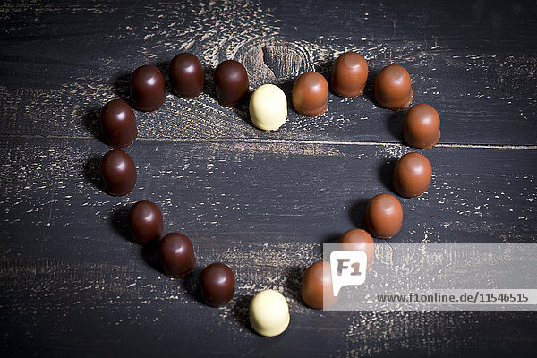 Verschiedene Marshmallows aus Schokolade bilden ein Herz auf dunklem Holz