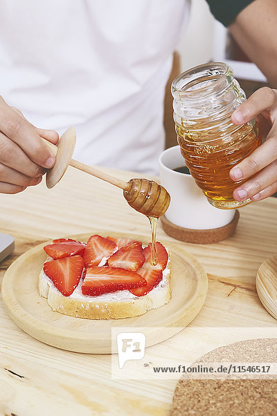 Junger Mann setzt Honig auf Toast mit Erdbeeren