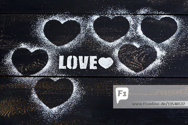Herzen und das Wort'Liebe' mit Puderzucker auf dunklem Holz geschabt