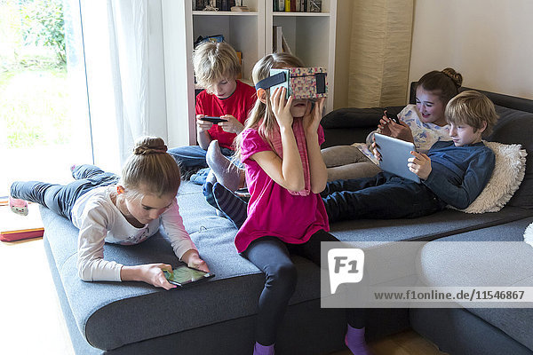 Fünf Kinder auf einer Couch mit verschiedenen digitalen Geräten