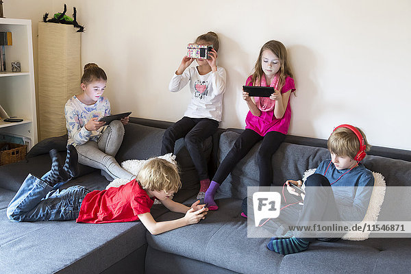 Five children on a couch using different digital devices