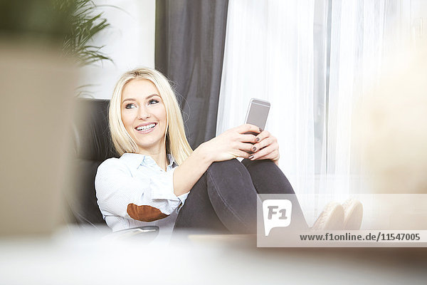 Portrait of smiling blond woman sitting at desk with her smartphone