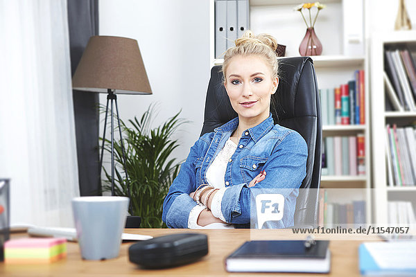 Portrait of confident blond businesswoman sitting at desk in her home office