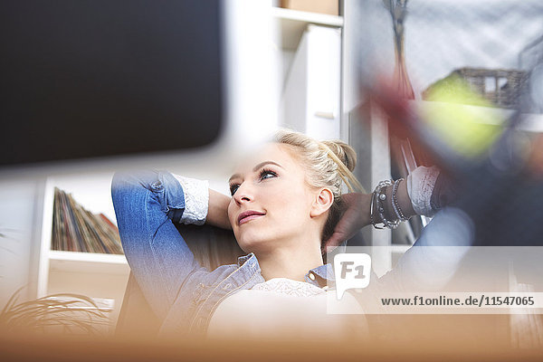 Smiling blond woman relaxing with hands behind her head at desk in the office