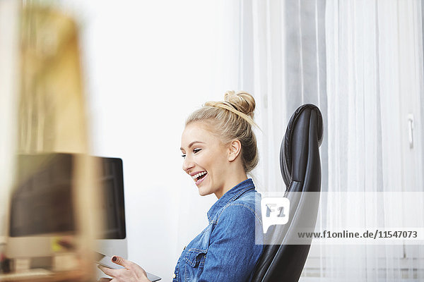 Laughing blond woman sitting at desk using digital tablet
