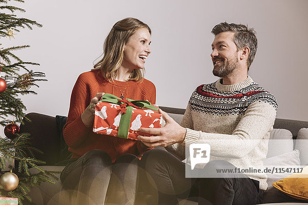 Paar tauscht ein Weihnachtsgeschenk auf dem Sofa aus