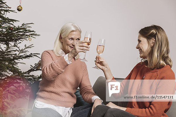 Senior woman and younger woman clinking glasses by Christmas tree