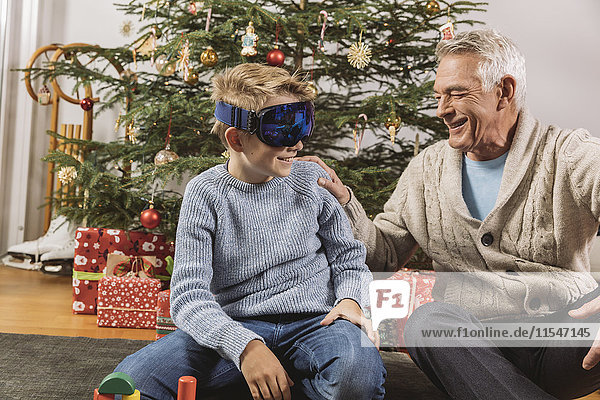 Glücklicher Großvater beim Anblick der neuen Skibrille des Enkels vor dem Weihnachtsbaum