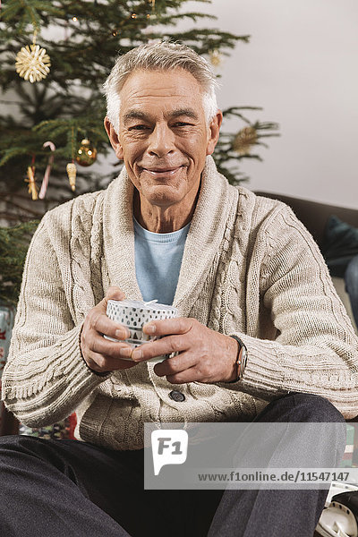 Porträt eines älteren Mannes mit Weihnachtsgeschenk vor dem Baum sitzend