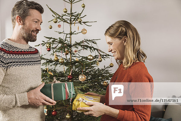 Paar tauscht Weihnachtsgeschenke vor dem Baum aus