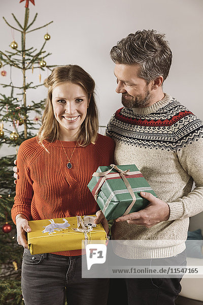 Paar mit Weihnachtsgeschenken vor dem Baum stehend