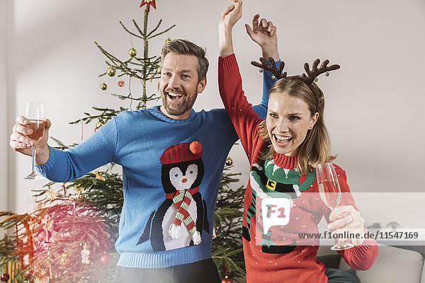 Zwei Menschen mit hässlichen Weihnachtspullovern tanzen vor dem Baum