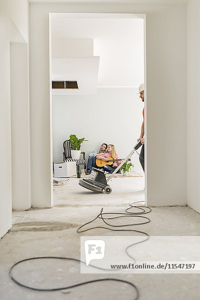 Ein Paar spielt Gitarre in seinem neuen Zuhause  während der Mann mit dem Grinder im Vordergrund arbeitet.