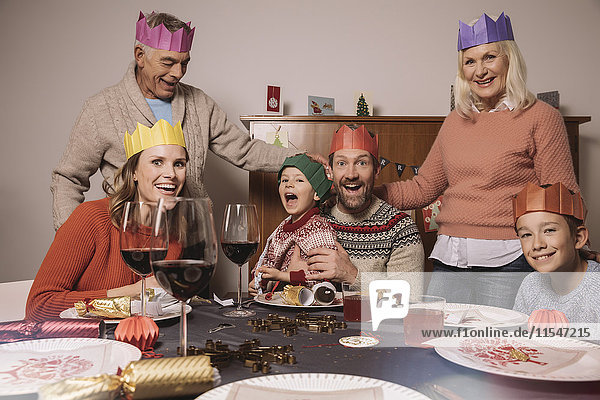 Funny three-generation family portrait with paper crowns during Christmas dinner
