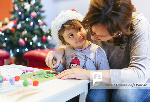 Mutter hilft ihrer kleinen Tochter beim Basteln Weihnachtsdekoration