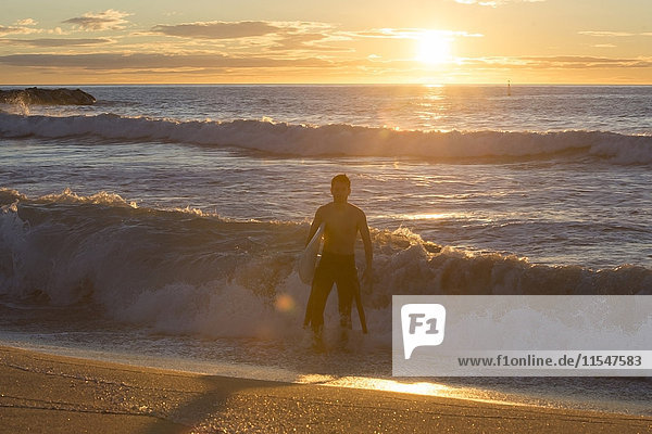 Surfer  der bei Sonnenaufgang aus dem Meer läuft