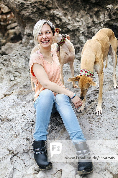 Spanien  Llanes  Porträt der lachenden jungen Frau mit ihren Windhunden am Strand