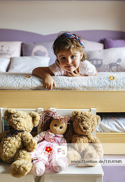 Porträt eines kleinen Mädchens auf dem Bett liegend mit Spielzeug im Vordergrund