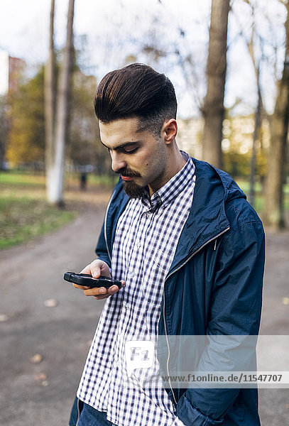 Junger Mann schaut auf sein Smartphone im Park