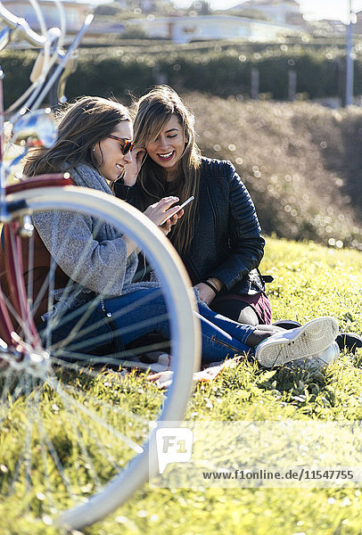 Zwei junge Frauen im Freien beim Musikhören mit dem Handy