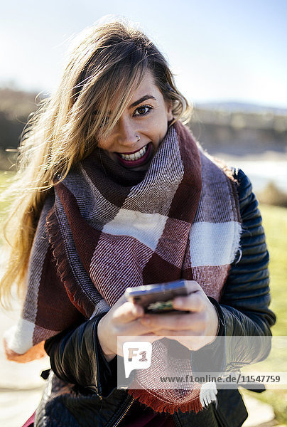 Porträt einer lächelnden jungen Frau mit Smartphone im Freien