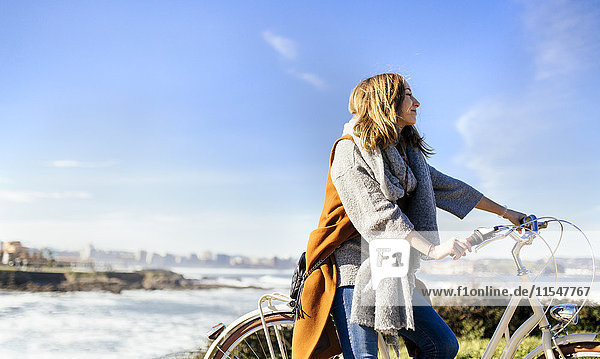 Spanien  Gijon  lächelnde junge Frau auf dem Fahrrad an der Küste