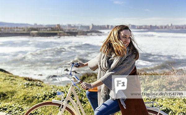 Spain  Gijon  happy young woman riding bicycle at the coast
