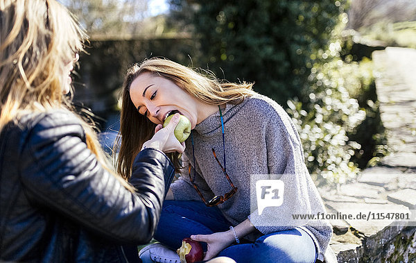 Zwei junge Frauen  die draußen Äpfel essen.