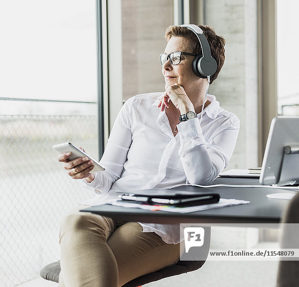 Businesswoman with cell phone and headphones in office