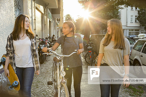 Three teenage girls on pavement with bicycle and skateboard