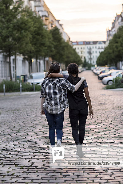 Two teenage girls walking on a street arm in arm