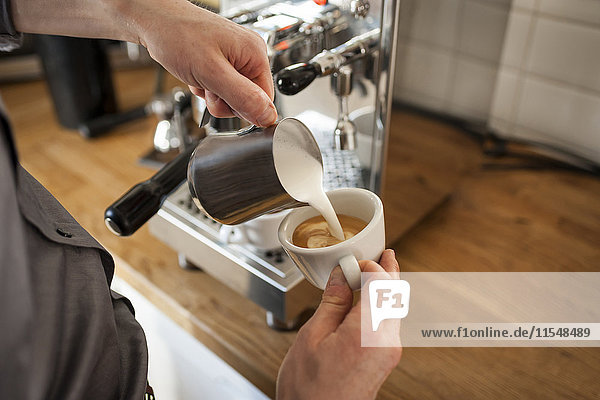Cappuccino  Mann gießt Milchschaum in die Kaffeetasse