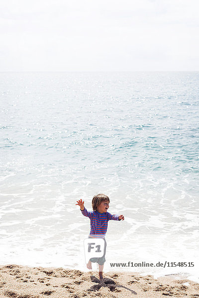 Fröhlicher kleiner Junge  der am Strand am Meer tanzt.
