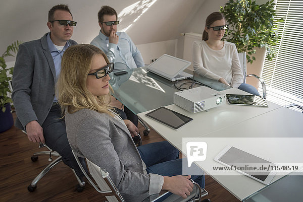 Vier Kollegen mit 3D-Brille bei einer Präsentation mit Projektor im Konferenzraum
