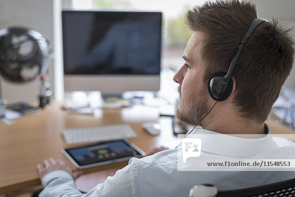 Young man at desk in office wearing headphones