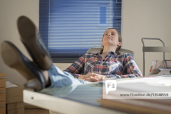 Junge Frau im Büro mit Füßen auf dem Schreibtisch und geschlossenen Augen