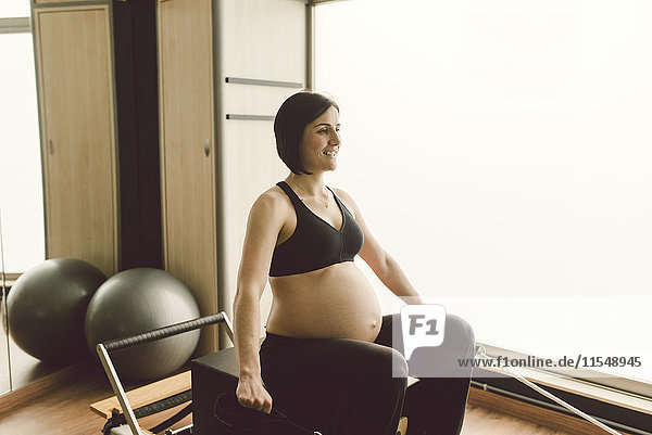 Schwangere Frau  die Pilates-Übungen mit einer Reformer-Pilates-Maschine in einem Fitnessstudio macht.