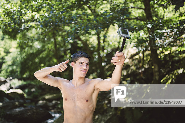 Shirtless young man filming himself with an action video camera in nature