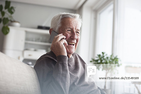 Porträt eines lachenden Senioren beim Telefonieren mit dem Smartphone zu Hause