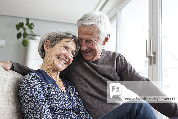 Fröhliches Seniorenpaar sitzt zusammen auf der Couch im Wohnzimmer
