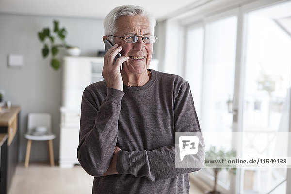 Porträt eines lächelnden älteren Mannes beim Telefonieren mit dem Smartphone zu Hause