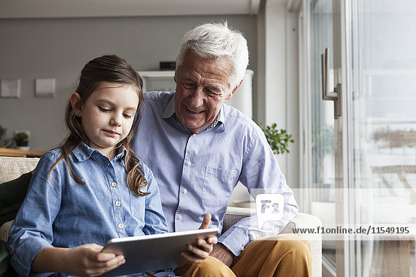 Großvater und seine Enkelin sitzen zusammen auf der Couch mit Hilfe eines digitalen Tabletts.
