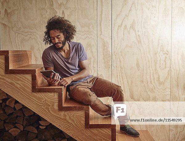 Young man on wooden stairs looking at digital tablet