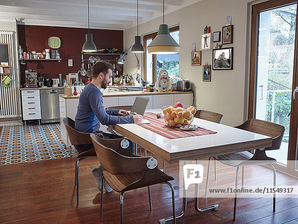 Young man using laptop in open plan kitchen