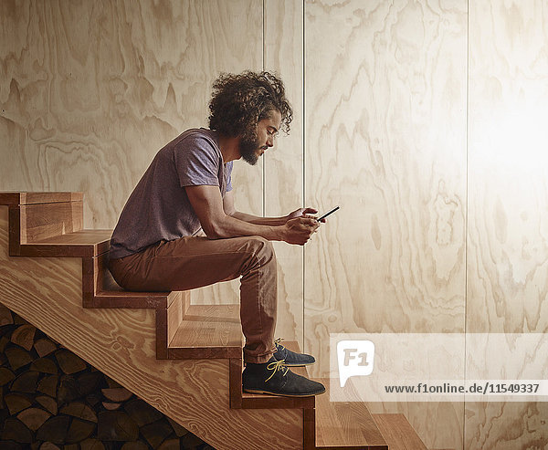 Young man sitting on wooden stairs looking at digital tablet